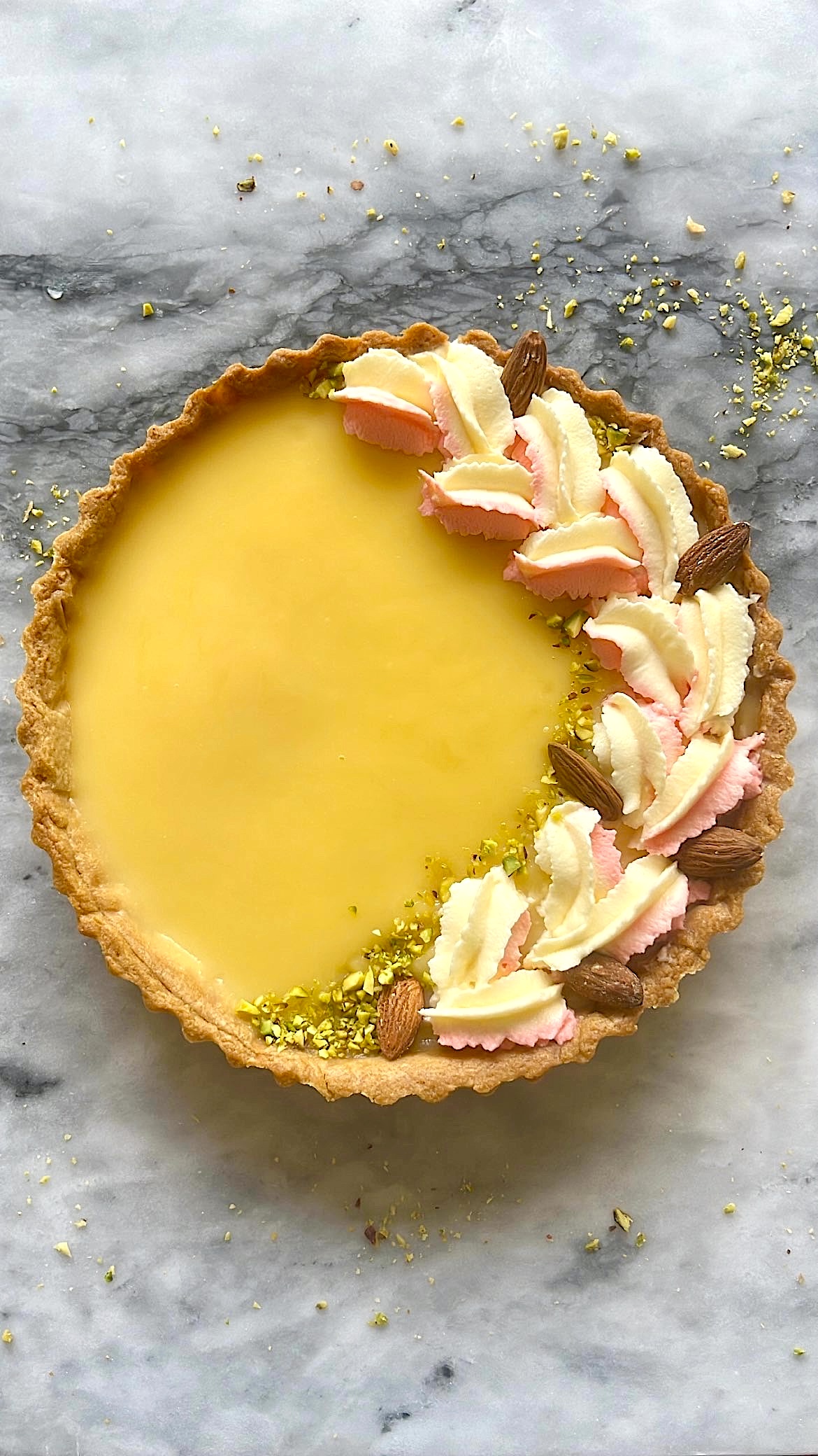 A lemon tart decorated with twilight-shaped cream, almond pieces, and pistachios on top.